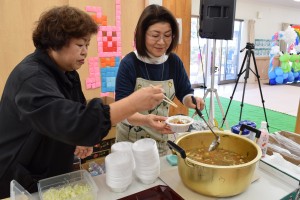 会場入り口ですいとんを振る舞う馬上さん（左）と平田さん（右）。具だくさんの汁とすいとんの美味しさに、おかわりをする人の姿も多く見られた